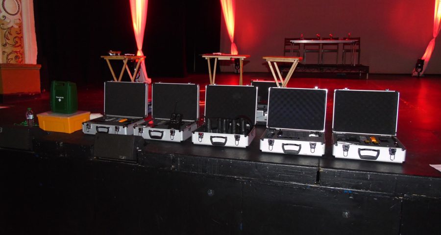 Ghost Hunting Equipment and Experiences. Ghost hunting equipment arranged on a dimly lit theatre stage, including EMF meter, digital voice recorder, flashlight, and camera. Ghost Hunting Equipment and Experiences: Your Essentials!